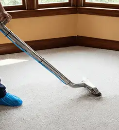 Steam carpet cleaning technician using a hot-water extraction wand on a residential carpet, wearing blue protective shoe covers Springfield, MO.