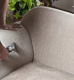Professional upholstery cleaner deep-cleaning a fabric sofa with a handheld extraction tool and hose Springfield, MO.